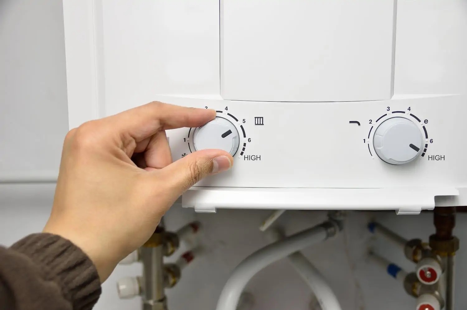 Person shown adjusting a dial on a tankless water heater to change the temperature setting